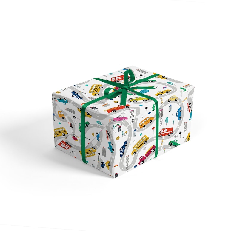 May include: A white gift wrap with a green ribbon. The wrapping paper features a repeating pattern of cars, buses, and trucks driving on winding roads. The cars are in various colors, including red, yellow, blue, and green.