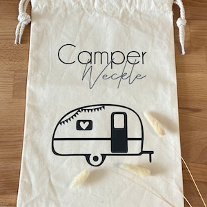 Könnte beinhalten: Eine weiße Canvas-Kordeltasche mit schwarzem Text, der "Camper Veckle" lautet, und einer schwarzen Silhouette eines Wohnwagens mit einem Herzen an der Seite.