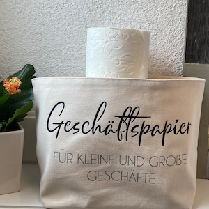 Könnte beinhalten: Eine beige Canvas-Tragetasche mit schwarzem Text, der "Geschäftspapier für kleine und große Geschäfte" lautet. Eine Rolle weißes Toilettenpapier liegt auf der Tasche.