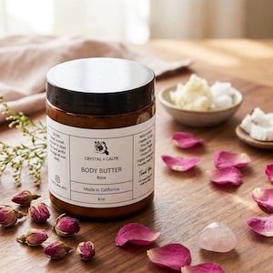 May include: An 8 oz amber glass jar of Crystal + Calyx Rose body butter with a black lid and white label. The label features the brand name, product type, and ingredients. It is surrounded by dried rosebuds, pink petals, and a rose quartz stone.