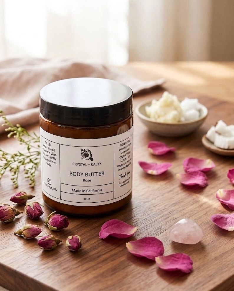 May include: An 8 oz amber glass jar of Crystal + Calyx Rose body butter with a black lid and white label. The label features the brand name, product type, and ingredients. It is surrounded by dried rosebuds, pink petals, and a rose quartz stone.