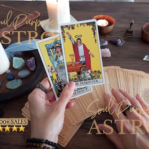 May include: Two tarot cards, The Magician and The Chariot, are held up. The Magician card features a figure in a red robe with a yellow background. The Chariot card shows a figure in blue armor. A deck of cards with a geometric back design lies below.