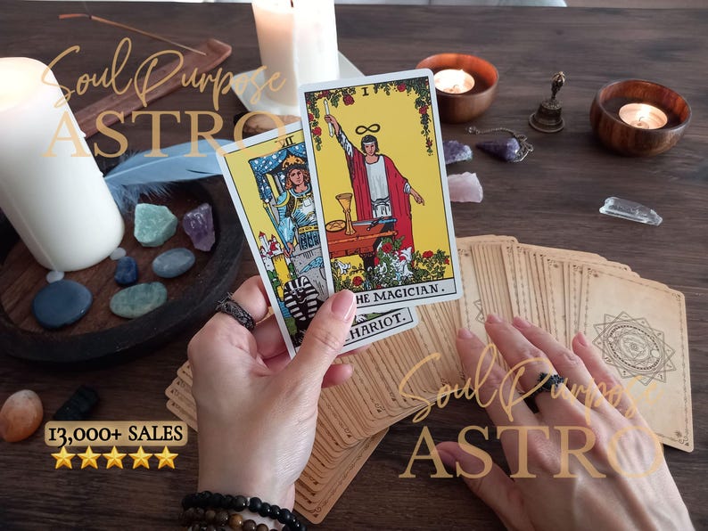 May include: Two tarot cards, The Magician and The Chariot, are held up. The Magician card features a figure in a red robe with a yellow background. The Chariot card shows a figure in blue armor. A deck of cards with a geometric back design lies below.
