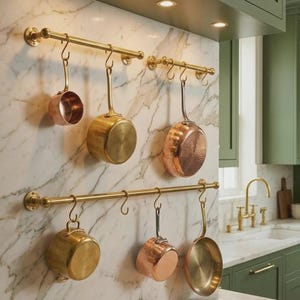 Peut inclure: Deux barres de suspension horizontales en laiton fixées au mur avec des crochets en S supportant une collection de casseroles et poêles en cuivre et laiton, disposées sur une crédence en marbre blanc veiné de gris dans une cuisine.