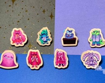Puede incluir: Ocho pines de madera con personajes de dibujos animados coloridos. Los personajes incluyen una niña rosa y blanca con un lazo, una criatura azul y verde con una corbata de moño, una criatura azul y blanca con un traje, un cocodrilo verde con un traje, una niña rosa y blanca con coletas, una niña rosa y blanca con coletas, una criatura rosa y blanca con una sonrisa y una niña rosa y blanca con coletas.