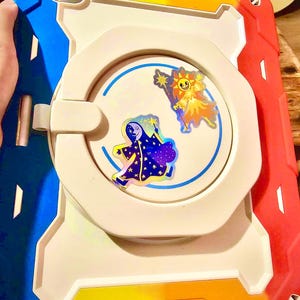 May include: A multi-colored tablet case with a white center and a blue, yellow, and red border. The case features two cartoon stickers of a sun and a moon. The case is designed to protect a tablet.