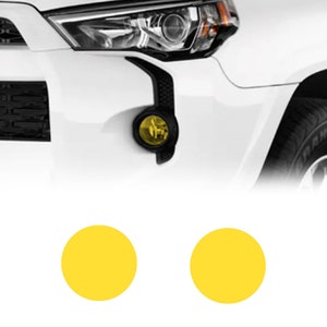 May include: A white car with two yellow fog lights. The fog lights are round and have a yellow tint.