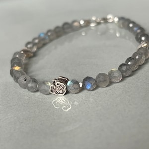 Op de afbeelding: Een grijze kralen armband met een zilveren bedel in de vorm van een wolk. De kralen zijn facetgeslepen en hebben een lichte iriserende glans.