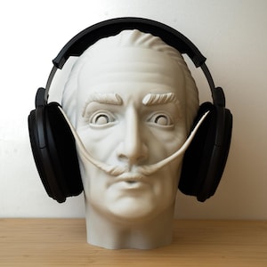 Puede incluir: Un busto de yeso blanco de un hombre con un bigote esculpido que lleva unos auriculares negros.