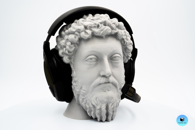 May include: A white bust of a man with a beard and curly hair wearing black headphones with a microphone. The bust is set against a white background.