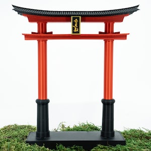 May include: A red and black traditional Japanese torii gate, a symbolic gateway to Shinto shrines. The gate is made of wood and has a black base. The top of the gate is decorated with a gold inscription.
