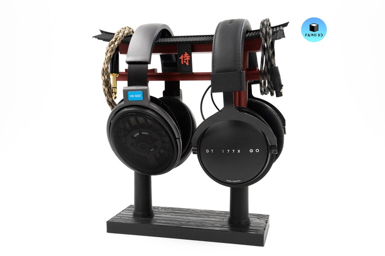 May include: A black headphone stand with two pairs of headphones. The stand has a red and black torii gate design. One pair of headphones is black with "HD 600" on the side, and the other is black with "DT 177X GO" on the side.