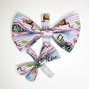 May include: Two purple and white bow ties with a frog and "Honeydukes" print. The larger bow tie has the name "Charlie" embroidered on it. The smaller bow tie has the name "Alfie" embroidered on it.