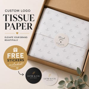 May include: A brown cardboard box containing white tissue paper with a repeating logo pattern, sealed with a round sticker reading thank you LUNE & CO. BOUTIQUE. Two additional circular stickers, one black and one white, feature the same brand logo.
