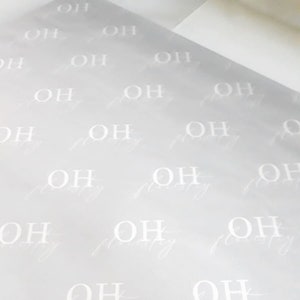 May include: A sheet of light gray wrapping paper with a repeating pattern of the letters "OH" in white.