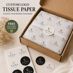 May include: A brown cardboard shipping box filled with white tissue paper featuring a repeating black Luna Jewelry logo with a crescent moon and stars. A round sticker with the same logo is centred on the paper, alongside a sheet of matching stickers.