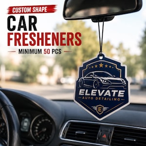 May include: A custom-shaped car air freshener hanging from a rearview mirror. The freshener is shield-shaped with a dark blue background, a white sports car graphic, and the text ELEVATE AUTO DETAILING with a gold E emblem at the bottom.