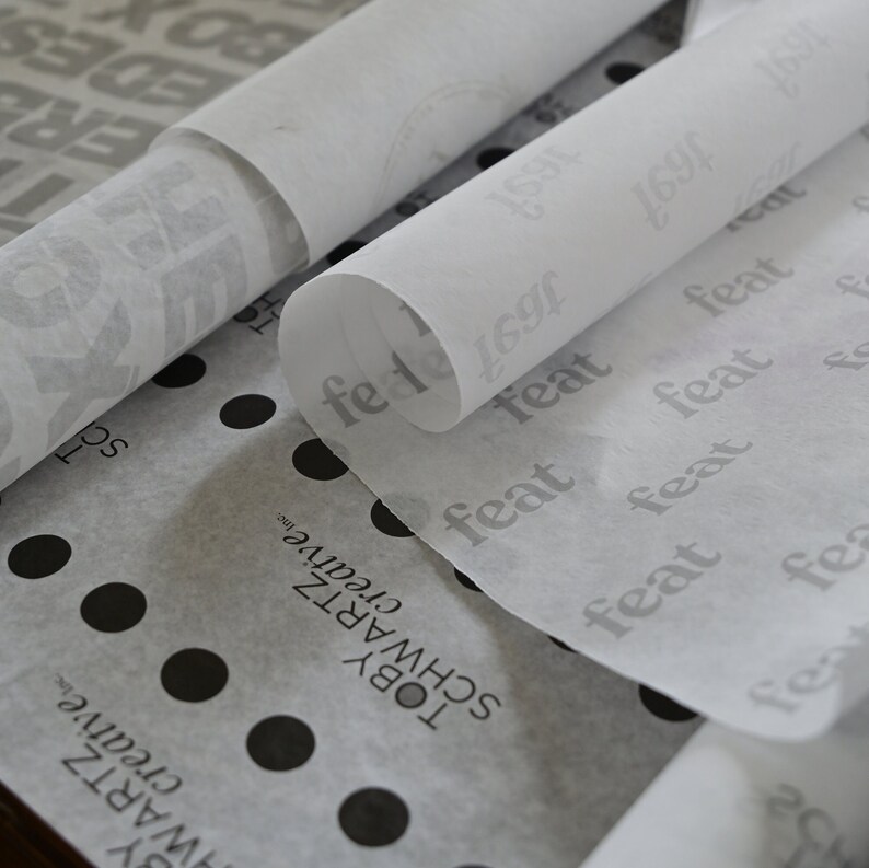May include: Close-up of white tissue paper rolls with the word "feat" printed repeatedly in gray. The tissue paper is layered on top of a white and black polka dot tissue paper with the text "TOBY SCHWARTZ creative inc."