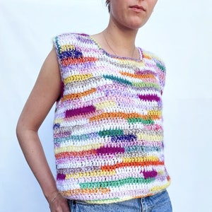 Puede incluir: Un top de crochet colorido con un diseño sin mangas. El top presenta una variedad de colores, incluyendo rosa, naranja, amarillo, verde y morado. El top está hecho con un hilo grueso y tiene un ajuste holgado.