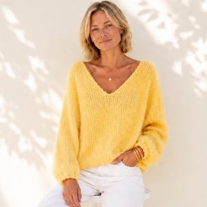 Può includere: Un maglione giallo brillante con scollo a V, maniche lunghe e ampie e una consistenza morbida e soffice, abbinato a pantaloni bianchi a gamba larga e semplici scarpe da ginnastica bianche. Il maglione presenta una vestibilità rilassata.