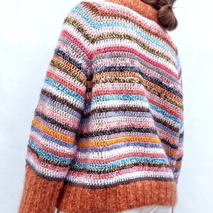 May include: A colourful striped crochet sweater with a brown fuzzy trim. The sweater is made with a variety of colours, including pink, blue, green, and yellow.