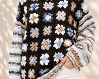 Könnte beinhalten: Ein langärmeliger Pullover mit dunkelbrauner Basis und einem wiederkehrenden Muster aus gehäkelten Blumenmotiven in Hellblau, Weiß und Beige. Die Ärmel haben ein horizontales Streifenstrickmuster in passenden Blau-, Weiß- und Brauntönen.