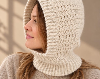 Puede incluir: Un pasamontañas de punto color crema con un borde acanalado a lo largo de la abertura facial y un patrón de puntos texturizados en el cuerpo principal. La prenda se extiende para cubrir el cuello con una base de cuello acanalado a juego.