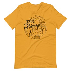 May include: A yellow t-shirt with a black graphic design that says "Life is better at Fort Wilderness". The graphic includes a sun, a lake, a tent, a campfire, a dock, and a tower with a flag.