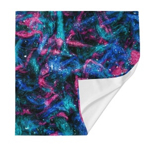 Op de afbeelding: Abstracte, door de galaxie geïnspireerde stof met draaiende blauwe, roze en turquoise kleuren. De stof heeft een glinsterende textuur en een witte achtergrond.
