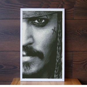 May include: A black and white close-up portrait of a man with a beard and a braid. He has a cross drawn on his cheek.