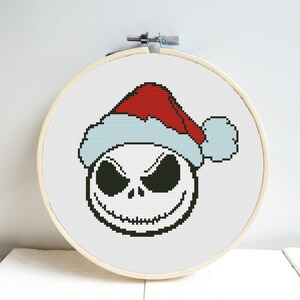 Puede incluir: Patrón de punto de cruz de Jack Skellington de Pesadilla antes de Navidad con un gorro de Papá Noel rojo y blanco.