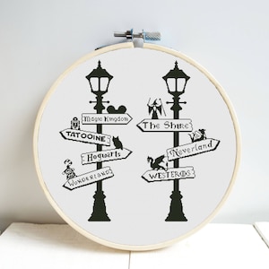 May include: Black and white cross-stitch pattern of two streetlights with signs pointing to different fictional locations, including "Magic Kingdom", "The Shire", "Tatooine", "Hogwarts", "Wonderland", "Neverland", and "Westeros".