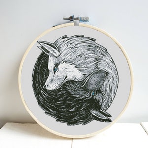 May include: A round embroidery hoop featuring a black and white wolf design. The artwork depicts two wolves in a yin-yang style, with one white and one black wolf. The wolves have blue eyes and are set against a light gray background.