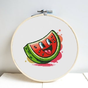 Puede incluir: Un patrón de punto de cruz de una rebanada de sandía sonriente con un interior rojo, una cáscara verde y un fondo rosa.
