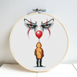 Può includere: Schema di punto croce di un viso di clown con un palloncino rosso e un bambino con un impermeabile giallo in piedi sotto.