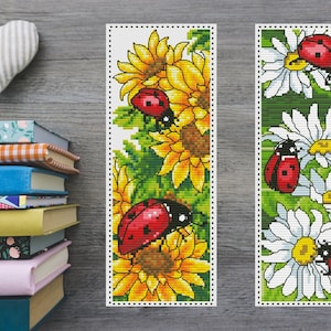 May include: Two cross-stitch bookmark designs featuring ladybugs on flowers. The first bookmark has ladybugs on sunflowers with green leaves. The second bookmark has ladybugs on white daisies with green leaves.