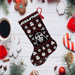 Könnte beinhalten: Ein schwarzer Weihnachtsstrumpf mit einem rot-weißen Strickmuster, das Star Wars-Charaktere wie Darth Vader, R2-D2 und Stormtrooper zeigt. Der Strumpf trägt den Namen "Sebastian".