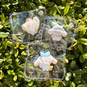 May include: Three clear plastic keyrings with cartoon character designs. One keyring features a white bunny with a pink bow, another a white character with a blue bow, and the last a white character with a blue bow and a small yellow bear.