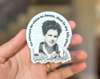 Puede incluir: Una pegatina con un retrato en escala de grises de San Carlo Acutis. La pegatina tiene un borde azul claro con el texto "To always be close to Jesus, that is my life plan" y "Saint Carlo Acutis" en cursiva.