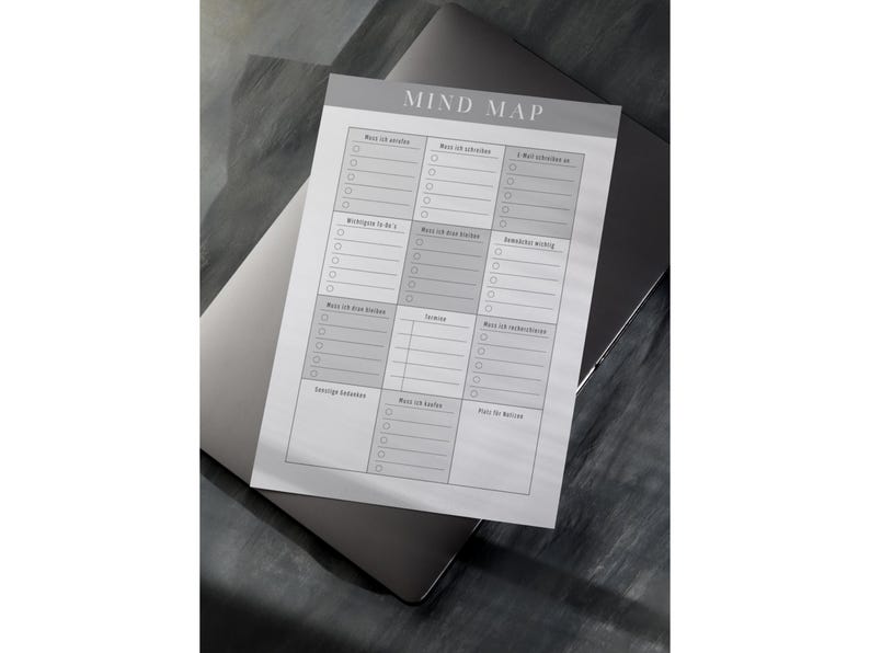 Peut inclure: Un bloc-notes de mind mapping gris et blanc avec le titre "MIND MAP" en haut. Le bloc-notes est pos&eacute; sur un ordinateur portable ferm&eacute;. Le bloc-notes comporte plusieurs sections avec des cases &agrave; cocher et des lignes pour &eacute;crire.