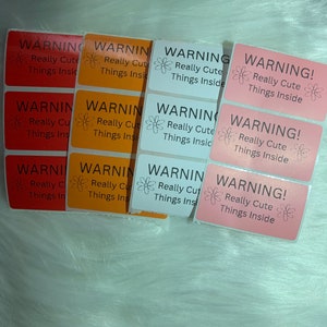 May include: A collection of rectangular stickers in various colors: red, orange, white, and pink. Each sticker has the word "WARNING!" above the text "Really Cute Things Inside" with a floral graphic.