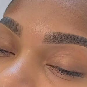 May include: Close-up of a person's face with perfectly shaped eyebrows. The eyebrows are dark brown and have a defined arch.