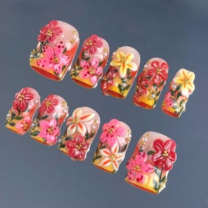 May include: A set of ten artificial nails, each adorned with a floral design. The nails feature a gradient of colors, from a light pink base to a vibrant orange at the tips. The flowers are in shades of pink, red, and yellow, with gold accents.