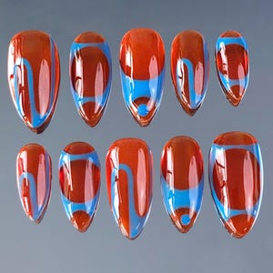 Op de afbeelding: Een set van tien amandelvormige kunstnagels. Elke nagel heeft een glanzende afwerking met een roodbruine basis en een ontwerp van blauwe en bruine wervelingen en strepen. De nagels zijn in twee rijen gerangschikt.