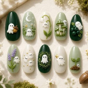 Puede incluir: Un juego de diez uñas postizas ovaladas con diseños en relieve 3D en tonos verde, blanco y crema. Las decoraciones incluyen pequeños fantasmas blancos, setas, lavanda, bayas, flores, una luna creciente y un diminuto brote verde.