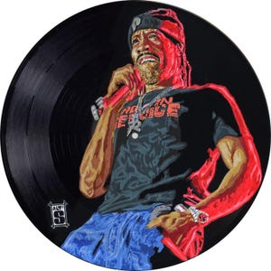 May include: A painted vinyl record featuring a portrait of a man holding a microphone. The man is wearing a black t-shirt with the words "INDEPENDENCE" in orange, blue jeans, and a silver chain. The record is black with visible grooves.