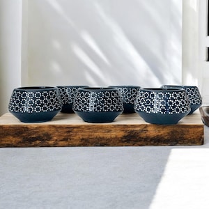May include: Six dark blue ceramic bowls with white dot patterns are arranged on a wooden plank. The bowls have a geometric shape and a matte finish. The bowls are suitable for serving food or as decorative items.