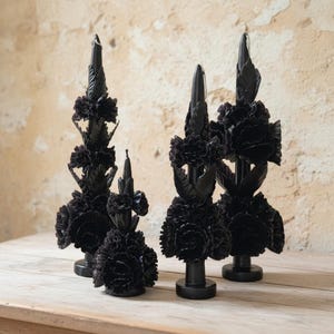 Puede incluir: Cuatro velas decorativas negras con diseños florales y de hojas. Las velas están dispuestas sobre una superficie de madera contra una pared texturizada. Las velas tienen una apariencia artística única, adecuada para la decoración del hogar.