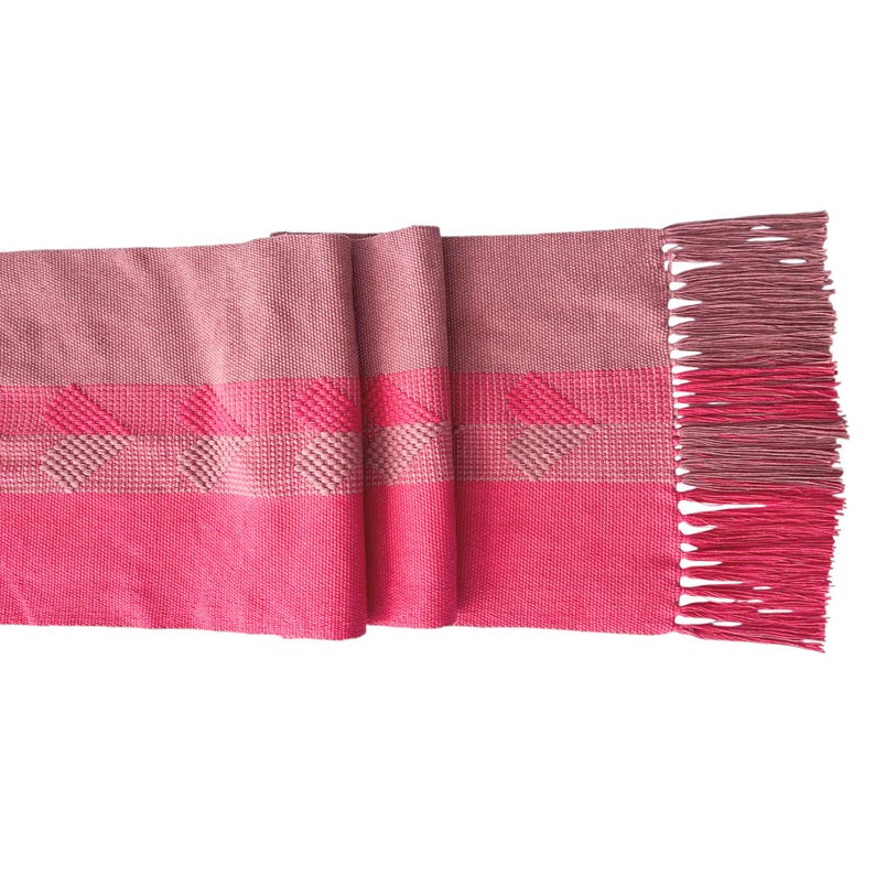 Op de afbeelding: Een geweven sjaal in roze en roze tinten. De sjaal heeft een gestreept patroon met een textuurontwerp en gefranjerde randen. Het kleurenpalet omvat lichte en donkere roze tinten.