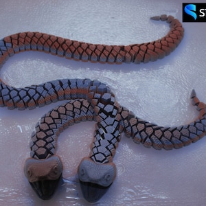 May include: Two-headed snake sculpture made of segmented, interlocking pieces. The snake is a light blue and brown colour, with a textured, scaly surface.